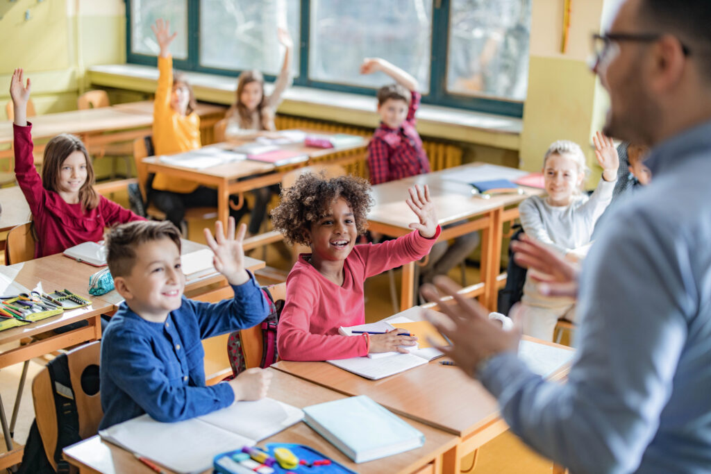 Elementary school children raise their hands in class.