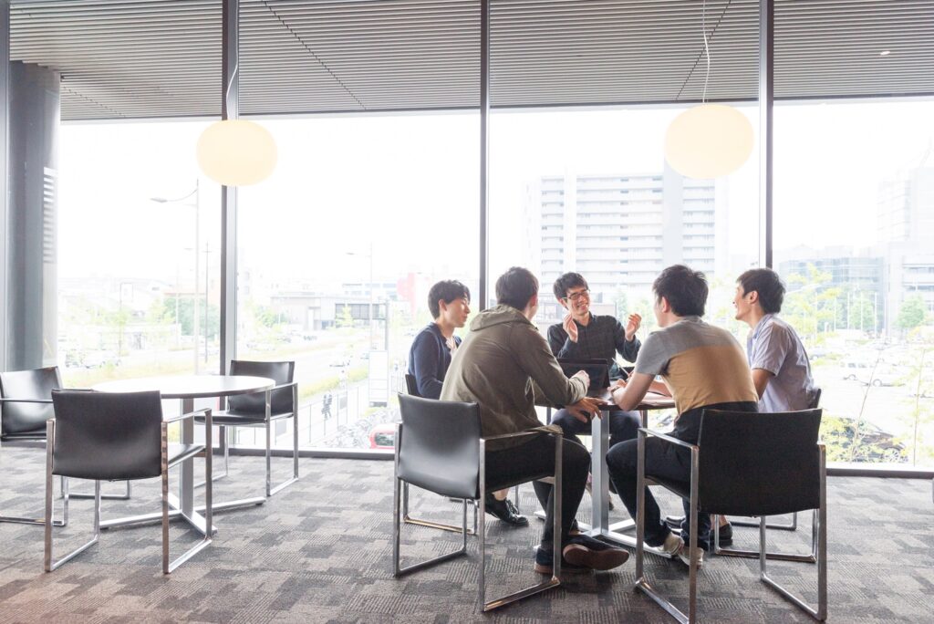 Five college students sitting at a table in a hallway outside a classroom.