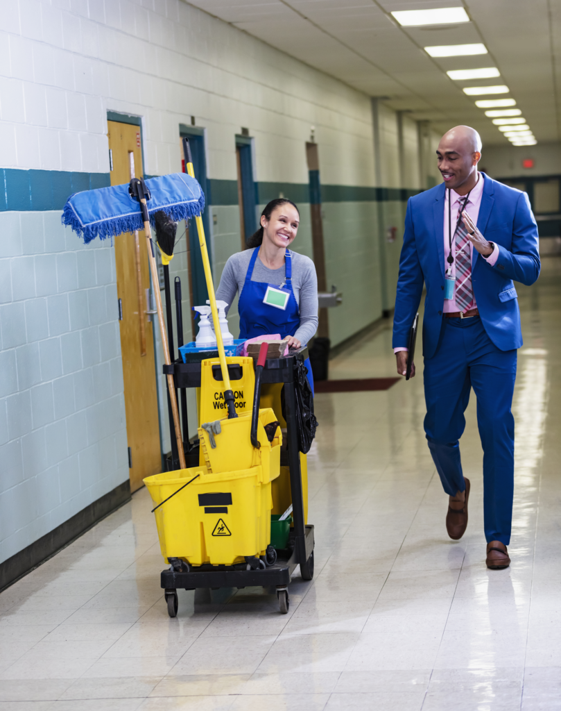 A janitor and teacher walk down the hall discussing their daily school cleaning checklist